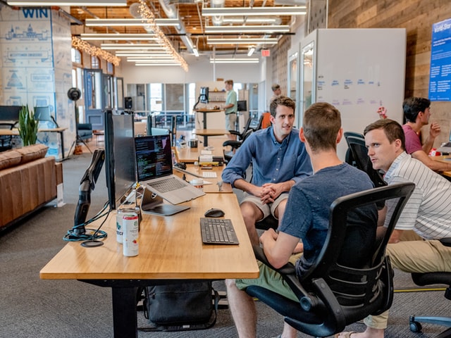 Three employees sitting on chairs in an office exchanging ideas